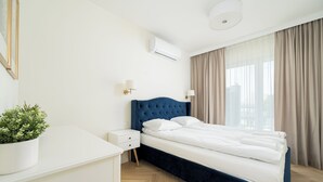 A hotel room with a bed, bedside tables, a potted plant, and a window with curtains.