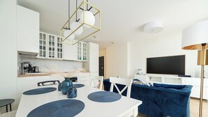 A modern kitchen with white cabinets, a dining table with blue placemats, a blue sofa, and a flat-screen TV.