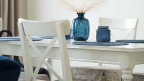 A dining area with a white table, chairs, a blue vase with dried plants, and a modern pendant light.