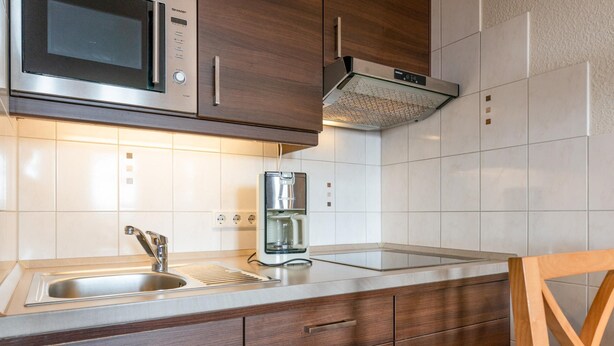 A kitchen with a stainless steel sink, a microwave, a coffee maker, and wooden cabinets. - Ferienwohnung Sellin auf Rugen mit Balkon (Sellin)