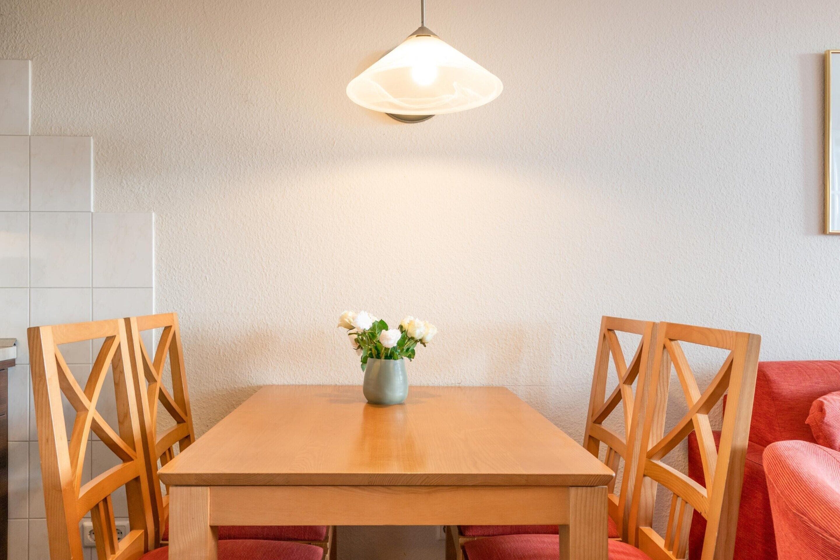 A dining table with chairs, a vase with flowers, and a hanging light fixture.