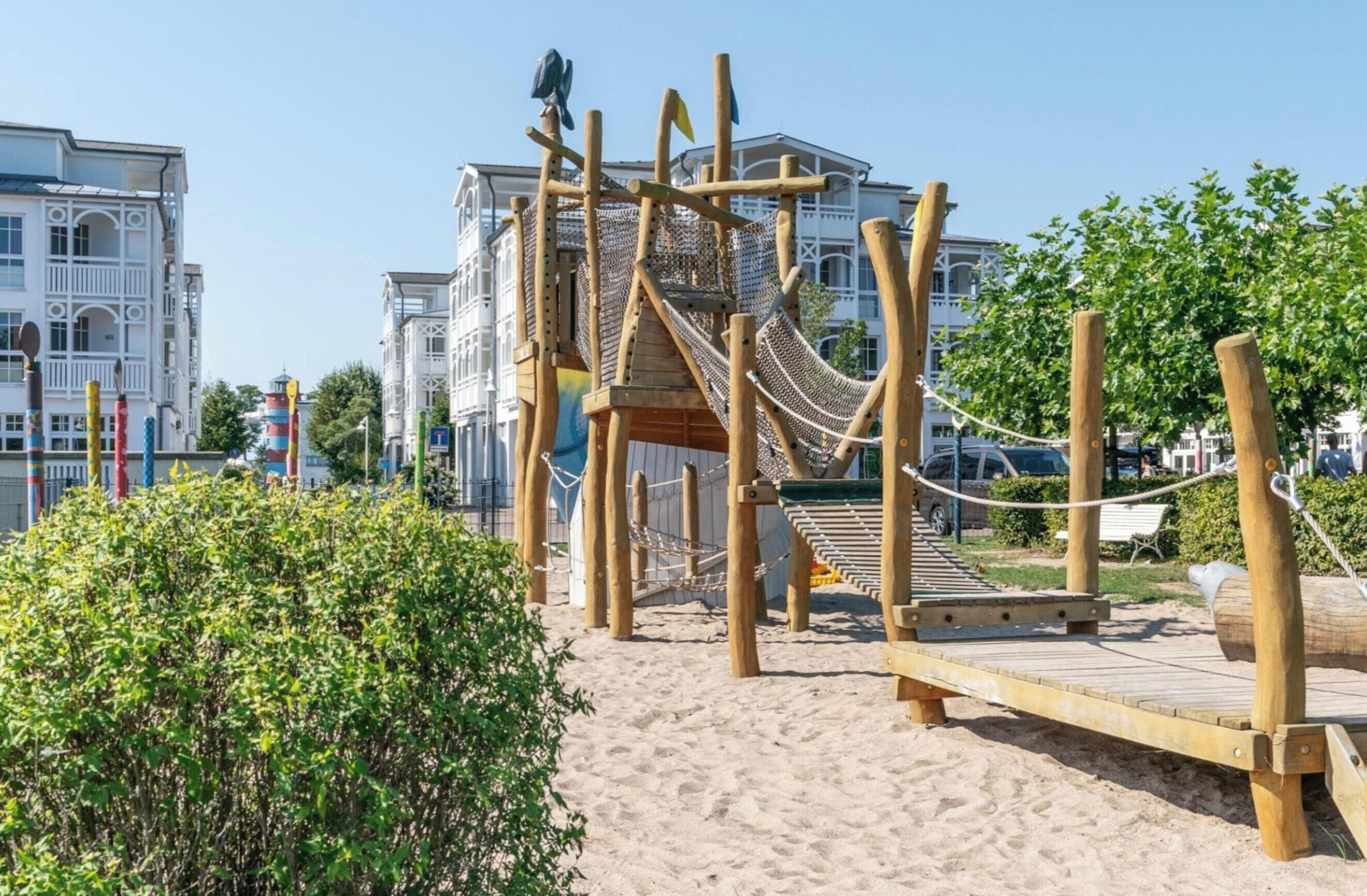 Estructura de madera para jugar con una escalera de cuerda y una plataforma, rodeada de arena y vegetación.