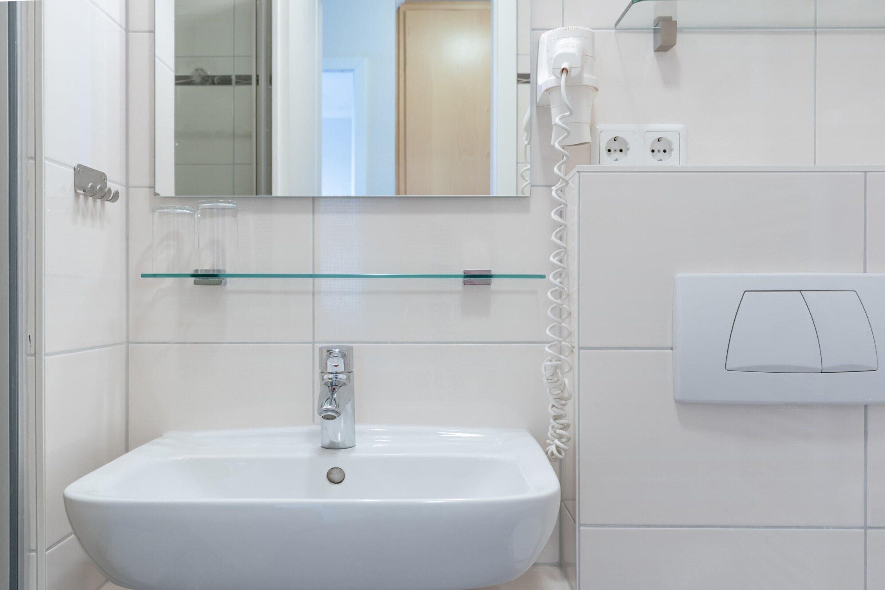 Un bagno con un lavandino bianco, uno scaffale in vetro, uno specchio, un telefono e un interruttore della luce.