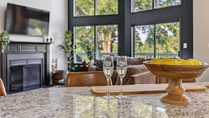 A kitchen with a granite countertop, two glasses, a wooden bowl with lemons, and a fireplace. - Fairway to Heaven: A-frame Retreat with Hot Tub, Arcade, Golf and More. Dogs OK. (Hedgesville)