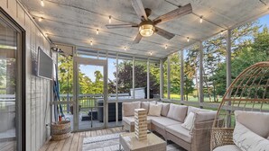 A covered outdoor seating area with a ceiling fan, a cushioned sofa, a coffee table, and a wicker chair. - Fairway to Heaven: A-frame Retreat with Hot Tub, Arcade, Golf and More. Dogs OK. (Hedgesville)