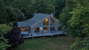 A house with a large deck, surrounded by trees. - Fairway to Heaven: A-frame Retreat with Hot Tub, Arcade, Golf and More. Dogs OK. (Hedgesville)