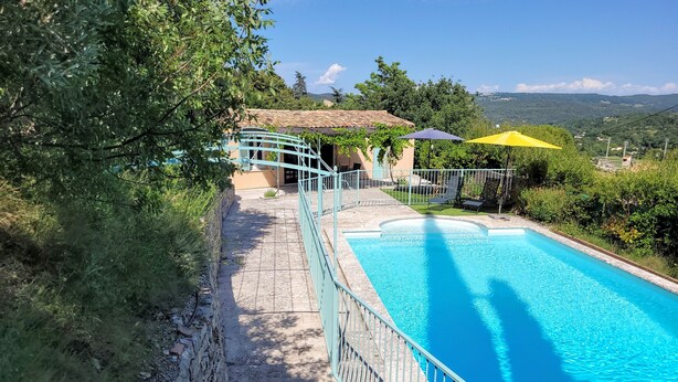 Una piscina con cerramiento azul, un edificio pequeño con techo de tejas y vistas del paisaje circundante.