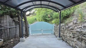 Un sendero cubierto que conduce a una entrada con puerta, bordeado por una valla de madera y un muro de piedra.