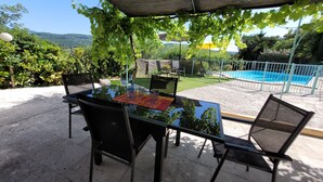 Mesa de vidrio con sillas bajo una pérgola, una piscina y vistas a las colinas.