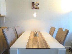 A dining table with four chairs, a wooden center panel, a hanging light fixture, and a framed picture on the wall. - Geschmackvoll Eingerichtete Ferienwohnung fur 4 im Seepark Sellin (Sellin)