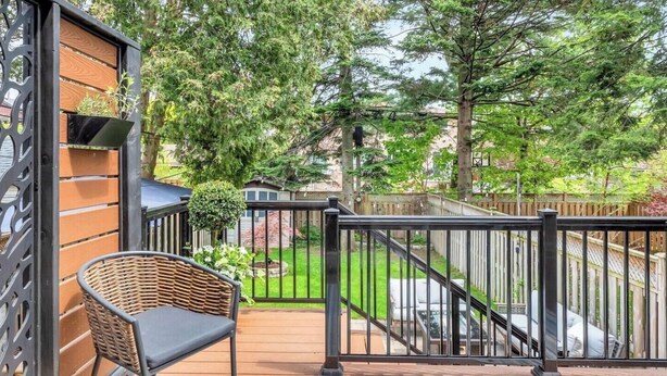 A deck with a wicker chair, a black metal railing, and a view of a backyard with a wooden fence and trees. - Charming, Family Friendly 3 bedroom House with Home Theatre near airport/transit (Toronto)
