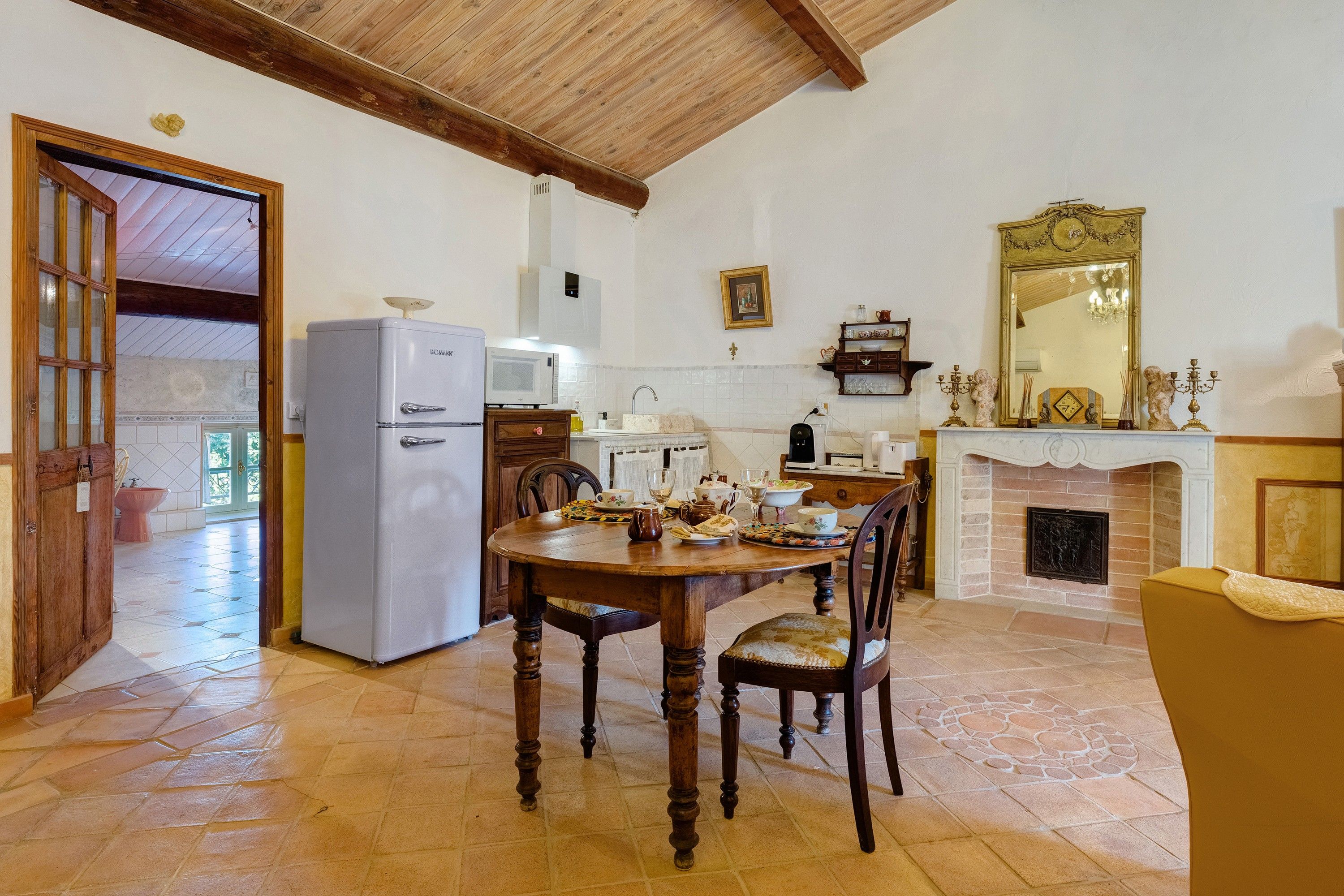 A dining area with a wooden table and chairs, a refrigerator, a microwave, and a fireplace.