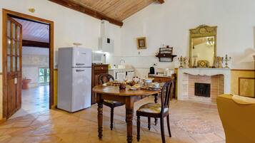 A dining area with a wooden table and chairs, a refrigerator, a microwave, and a fireplace.