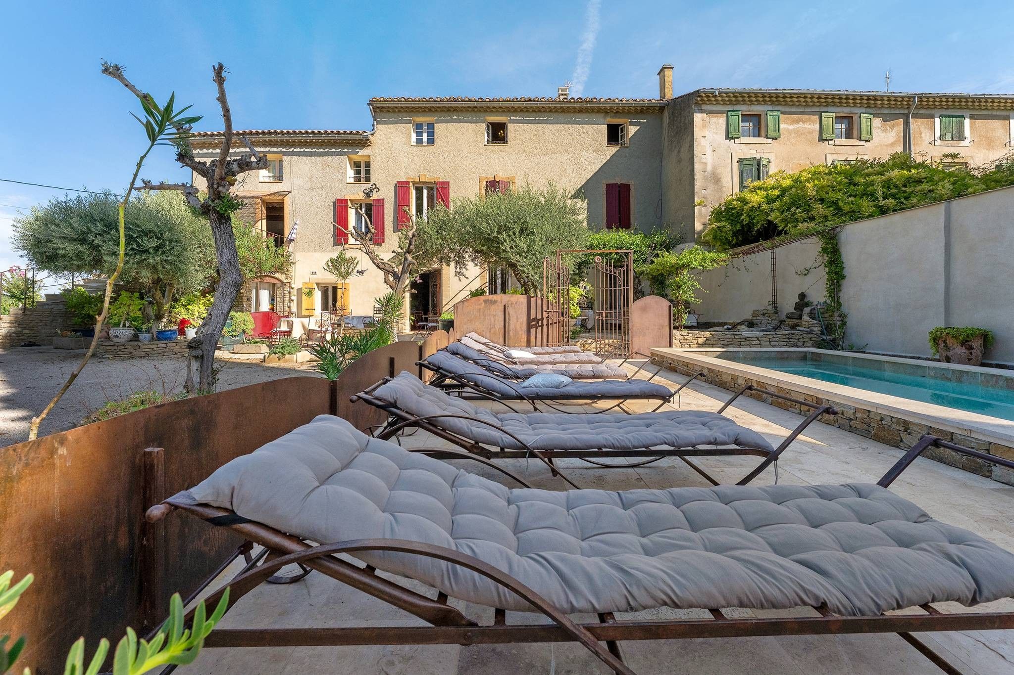 A poolside area with lounge chairs and a building with red shutters in the background.