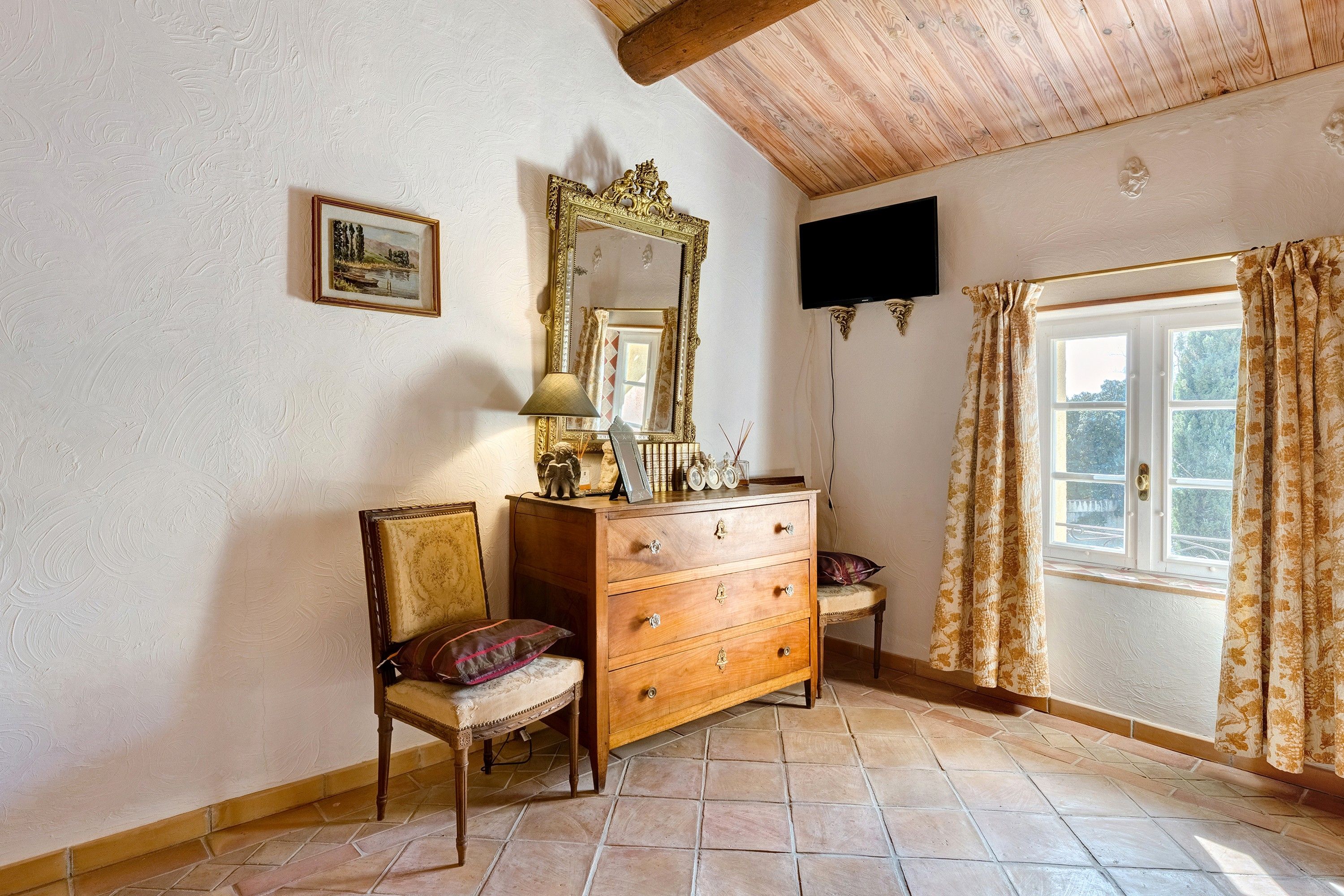 A room with a wooden dresser, a chair, a mirror, and a window with curtains.