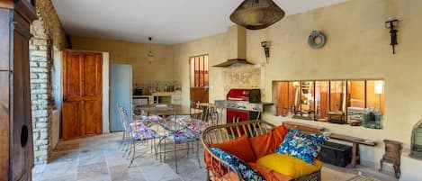 A rustic kitchen with a red grill, a dining area with wicker furniture, and a stone floor.