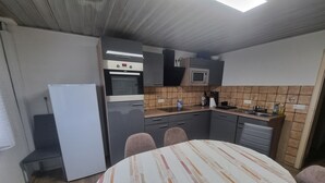 Ett kompakt kök med kylskåp, ugn, mikrovågsugn och en matplats med bord och stolar.