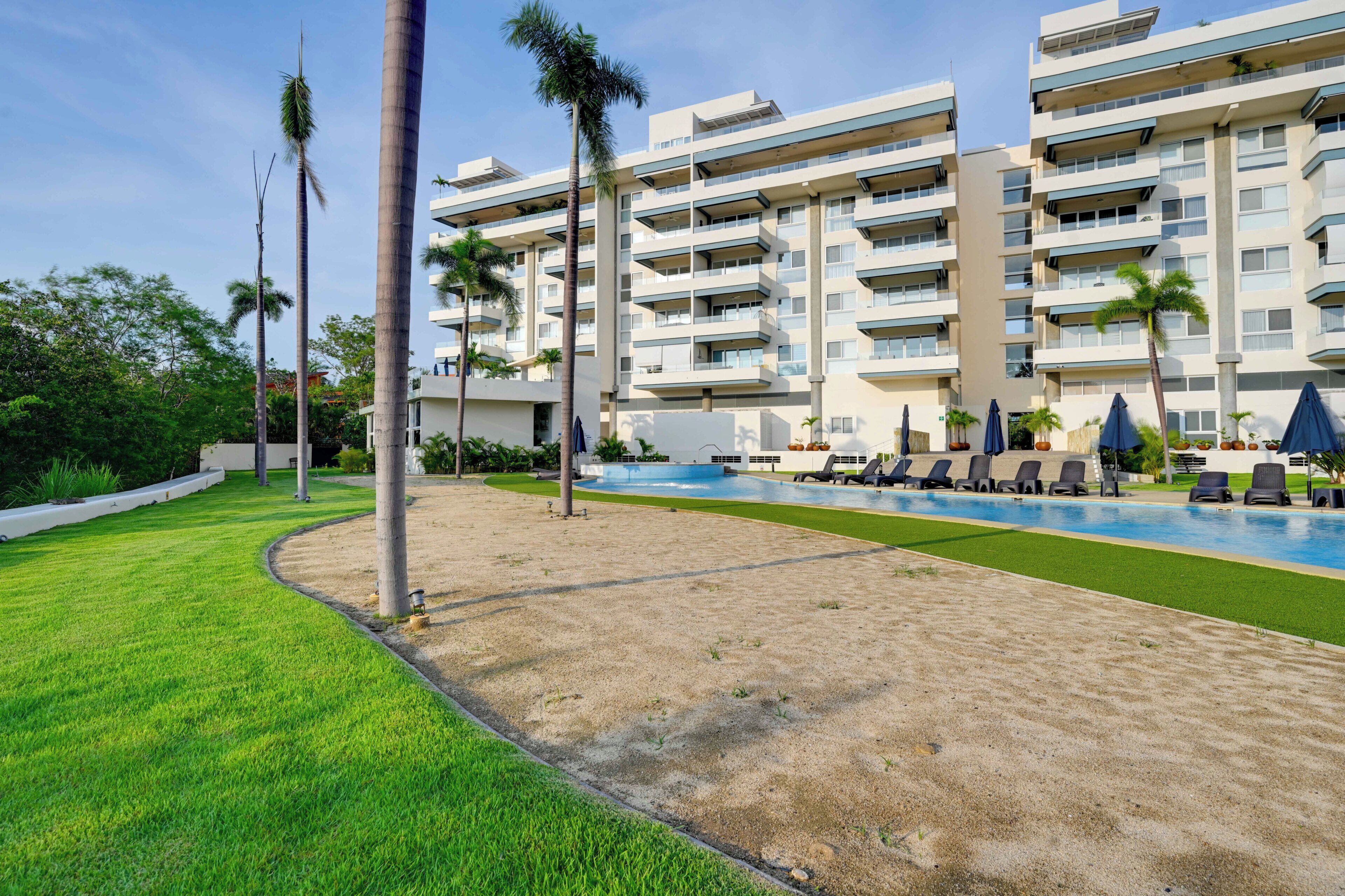 A modern hotel with a swimming pool, multiple balconies, and palm trees.