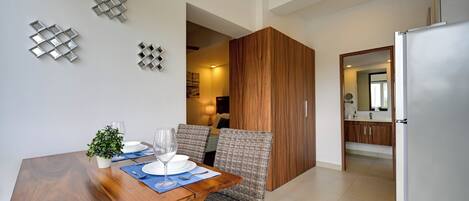 Un comedor con una mesa de madera, sillas y una planta pequeña en maceta. Hay decoraciones en la pared y se ve entrada a otra habitación.