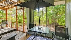 Un patio techado con una mesa y sillas, ventanas amplias y vistas a árboles.