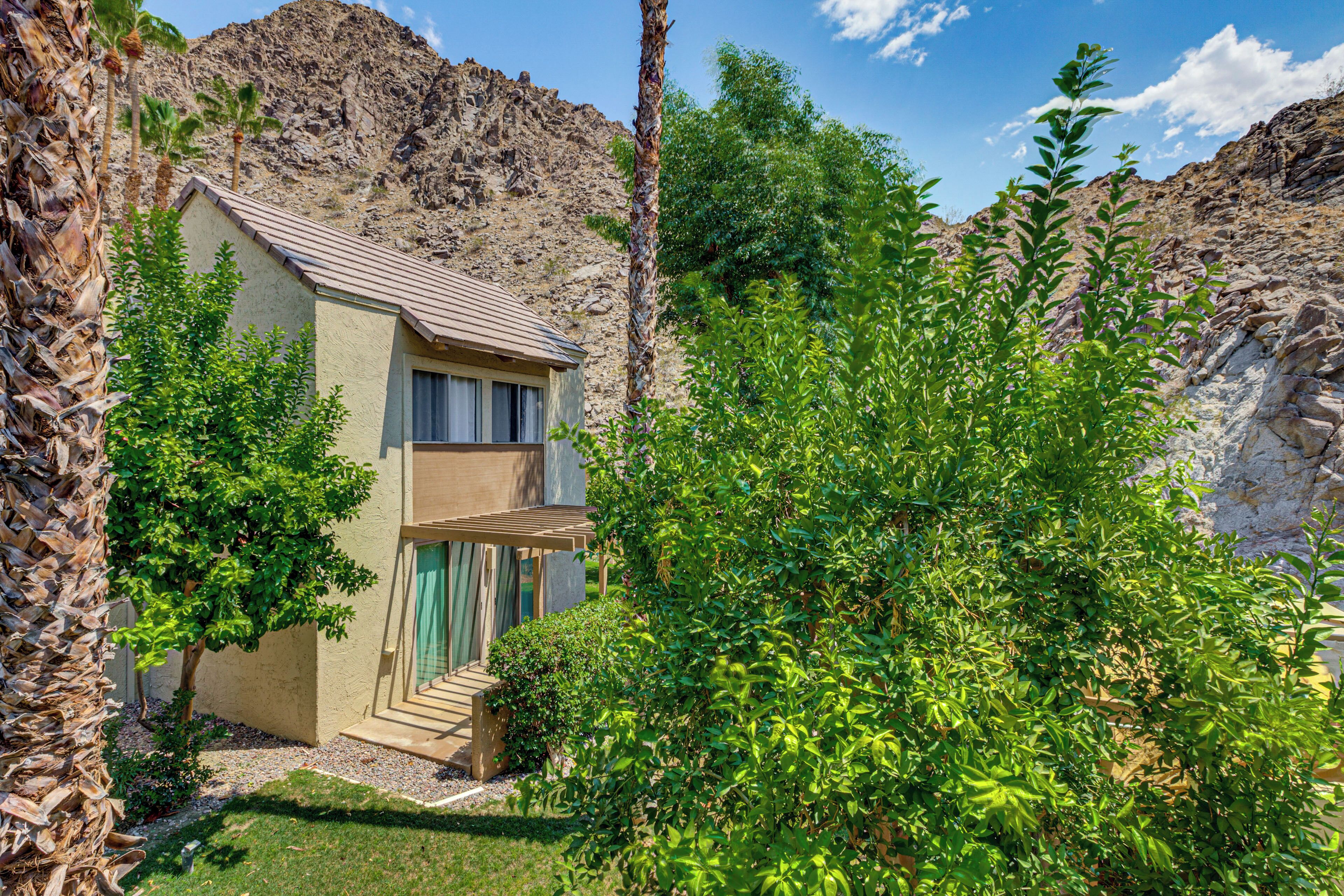 A two-story building with a balcony, surrounded by lush greenery and rocky terrain.
