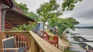 A wooden deck with a chair, a tree, and a view of a lake with docks.