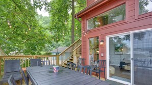 A wooden deck with a table and chairs, a staircase, and a glass door leading to an interior space.