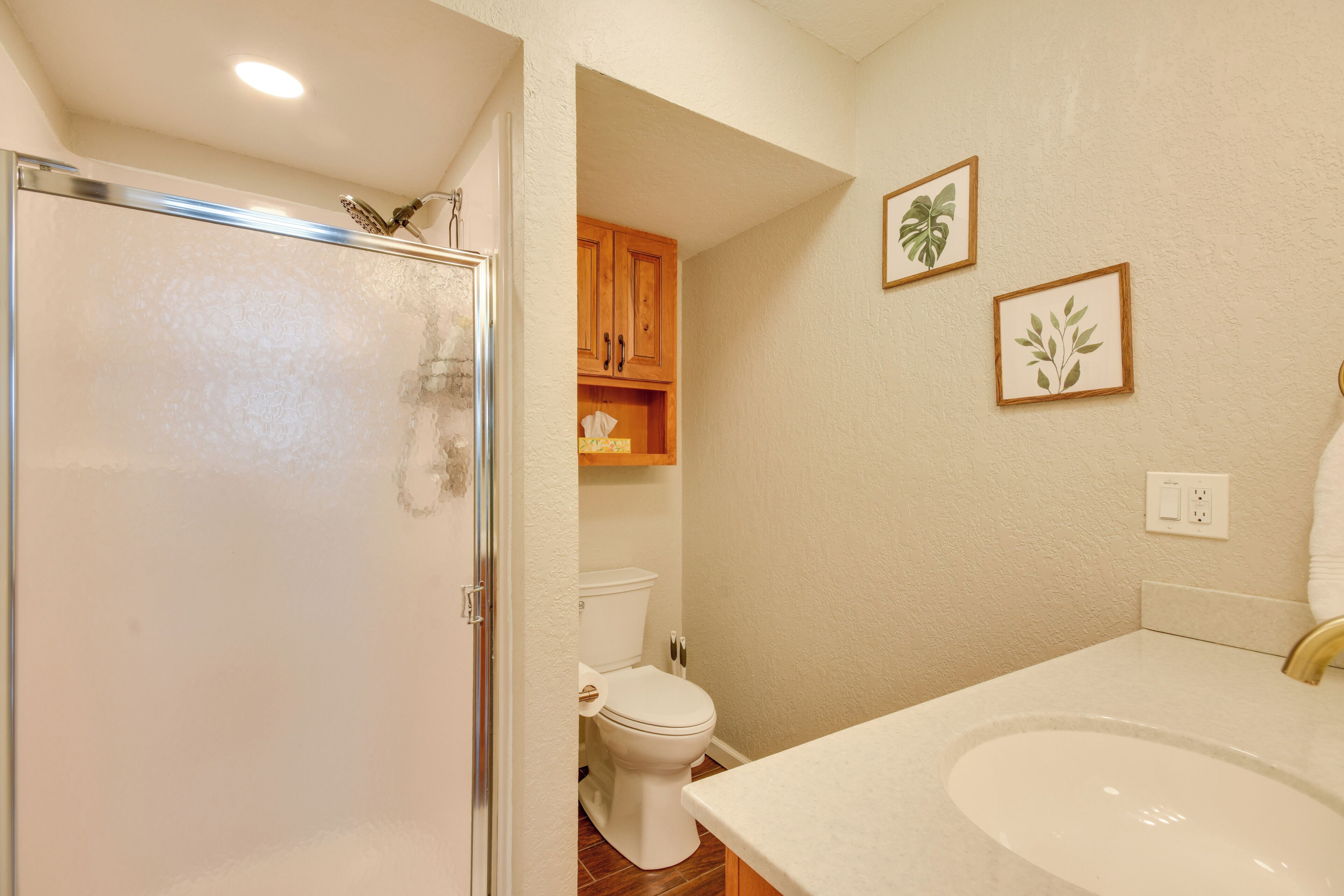 A bathroom with a shower, toilet, sink, and wooden cabinets.
