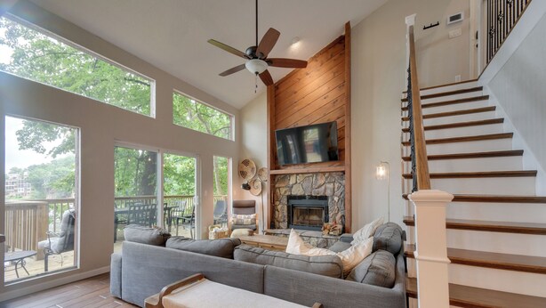 A spacious living area with a large gray sectional sofa, a fireplace, and a wooden staircase.