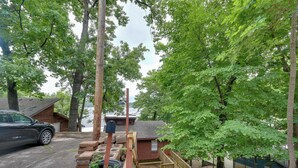 A wooden deck with a mailbox, a car parked nearby, and a building with a sloped roof in the background.