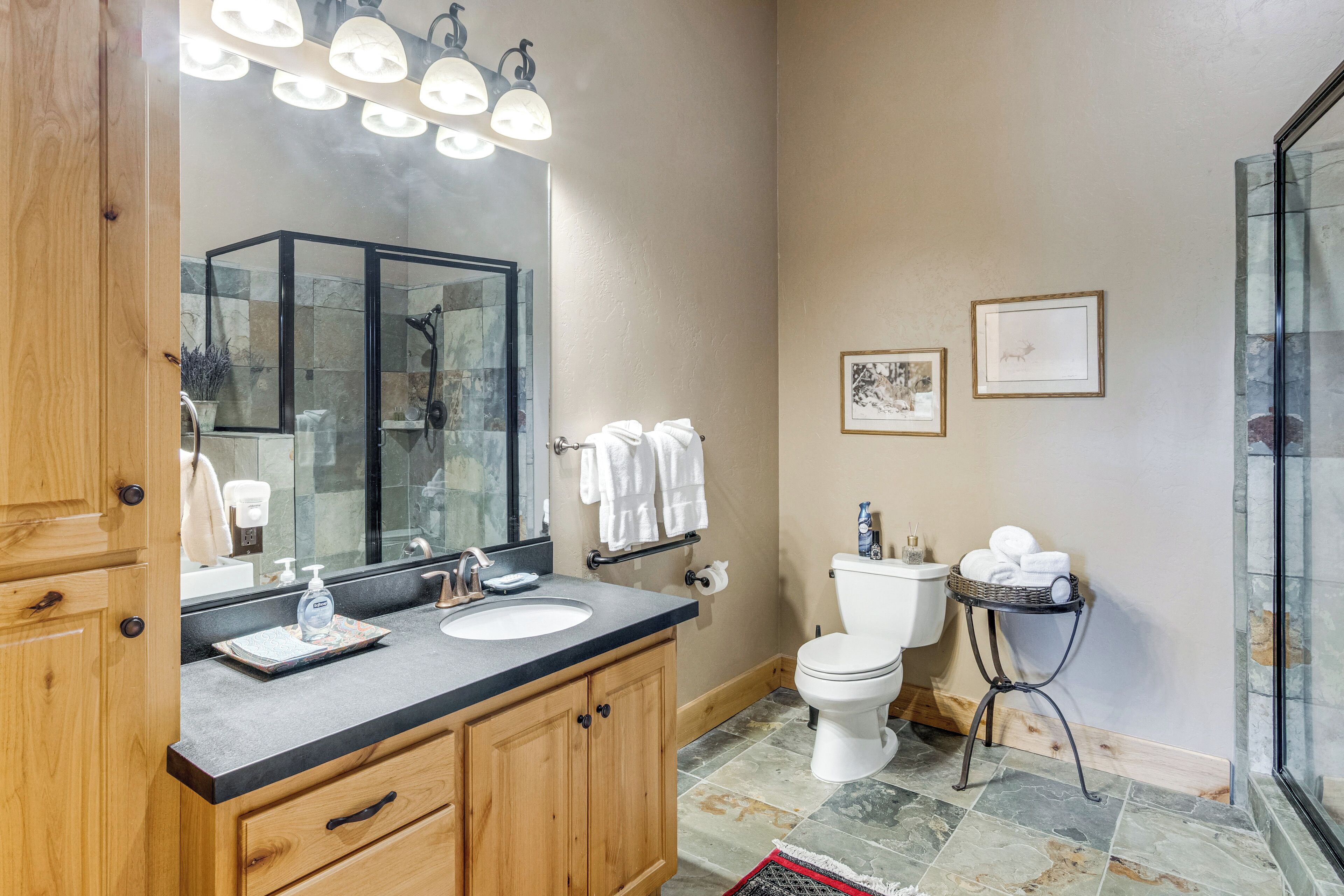 A bathroom with a wooden vanity, a large mirror, a sink, a toilet, and a glass shower enclosure.
