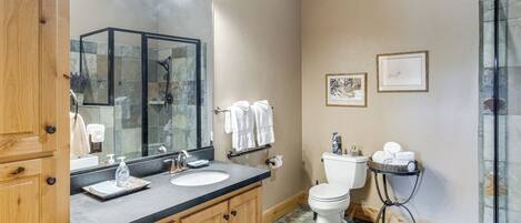 A bathroom with a wooden vanity, a large mirror, a sink, a toilet, and a glass shower enclosure.