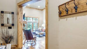 A wooden-framed doorway leading to a living room with a rocking chair, a mounted mirror, and a wall-mounted coat rack. - Gateway to the Teton Valley! Luxe Mtn Condo (Victor)