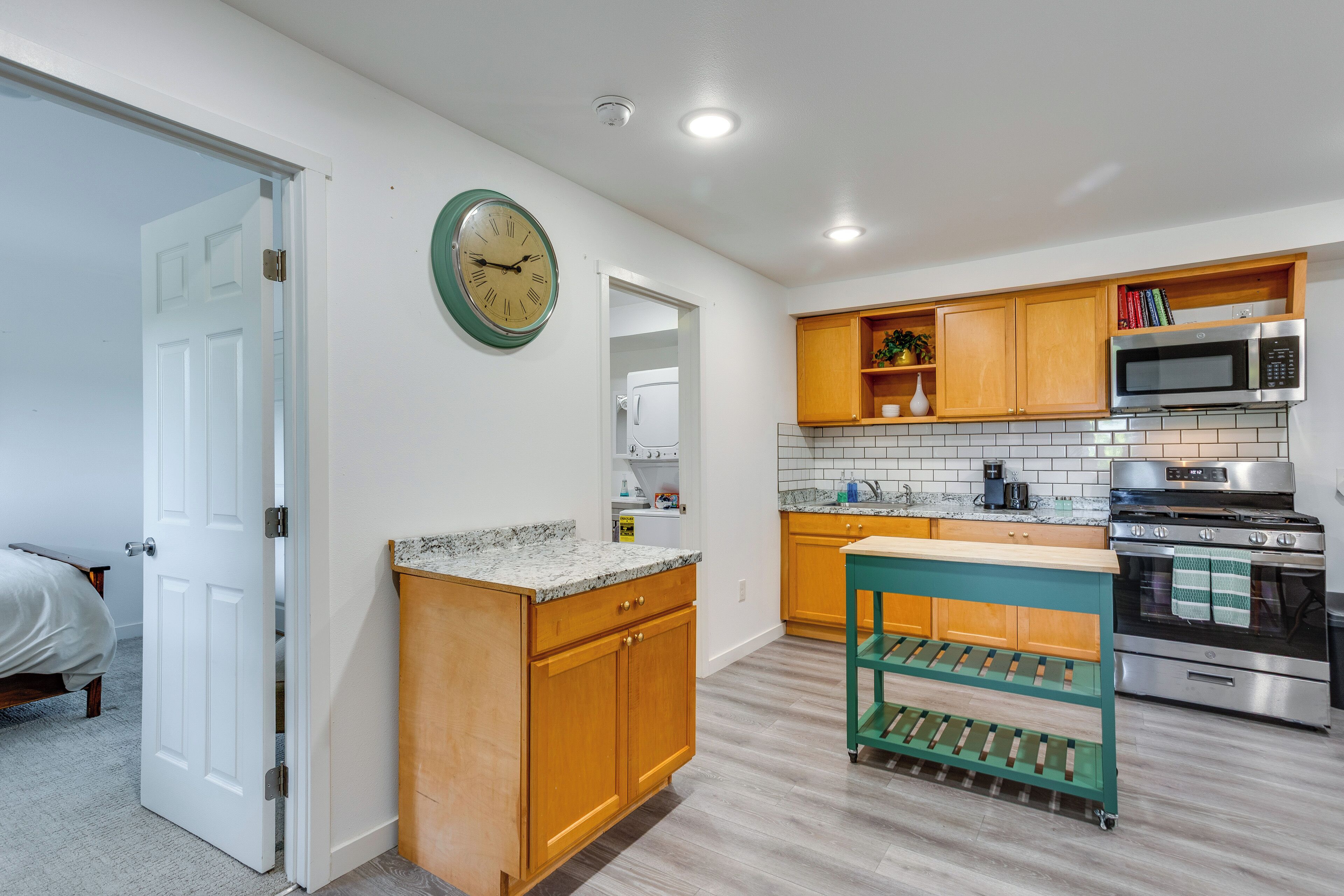 A kitchen with wooden cabinets, a microwave, an oven, a clock, and a green cart.