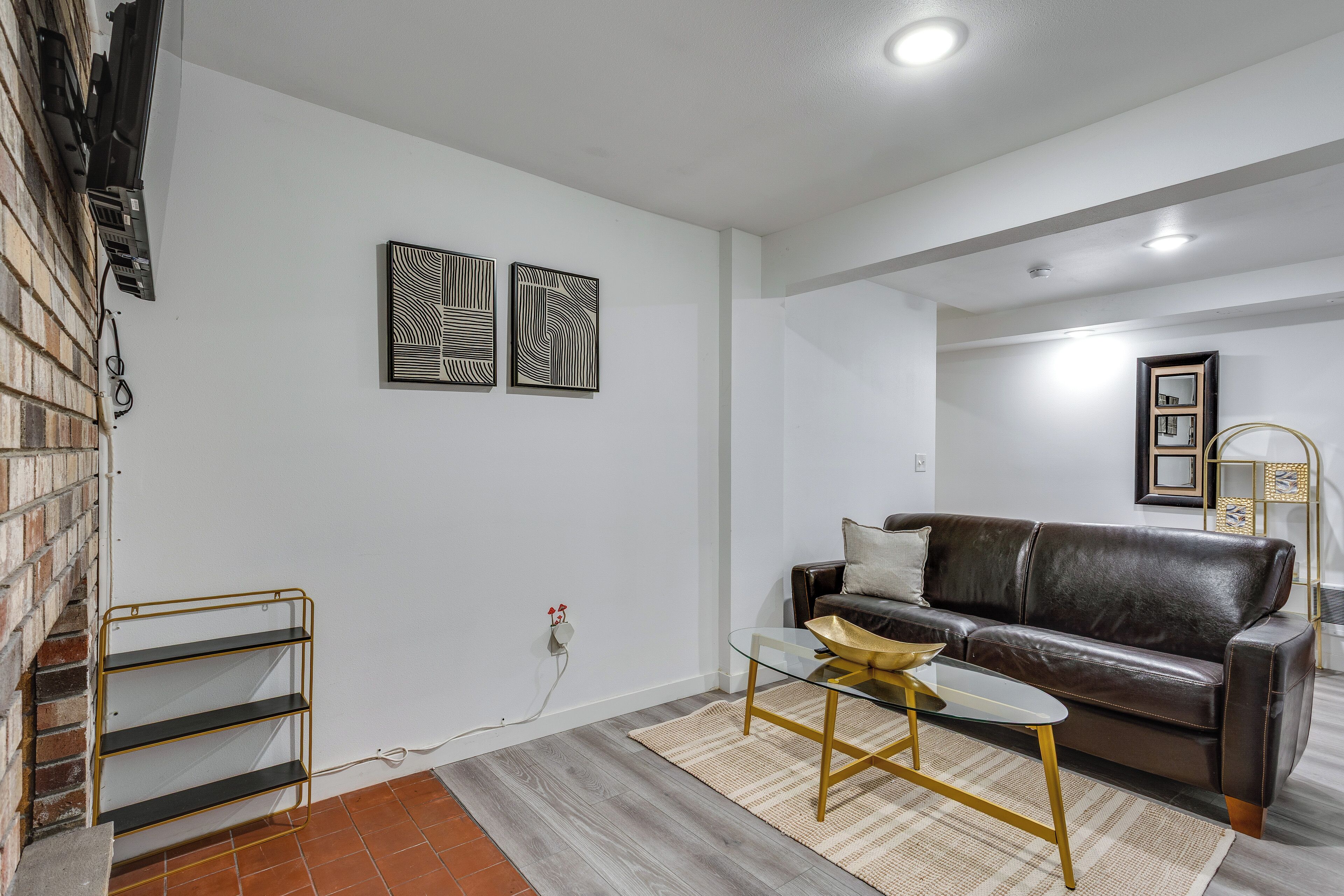 A living room with a brown leather sofa, a glass coffee table, and a brick wall.