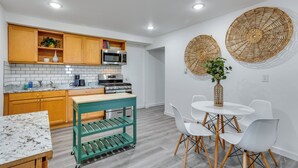 A modern kitchen with wooden cabinets, a built-in microwave, a stove, and a green cart. There is a round table with white chairs and a vase with a plant. - Quick Hwy Access to Seattle! Mtn-view Apt w/ Yard (Renton)