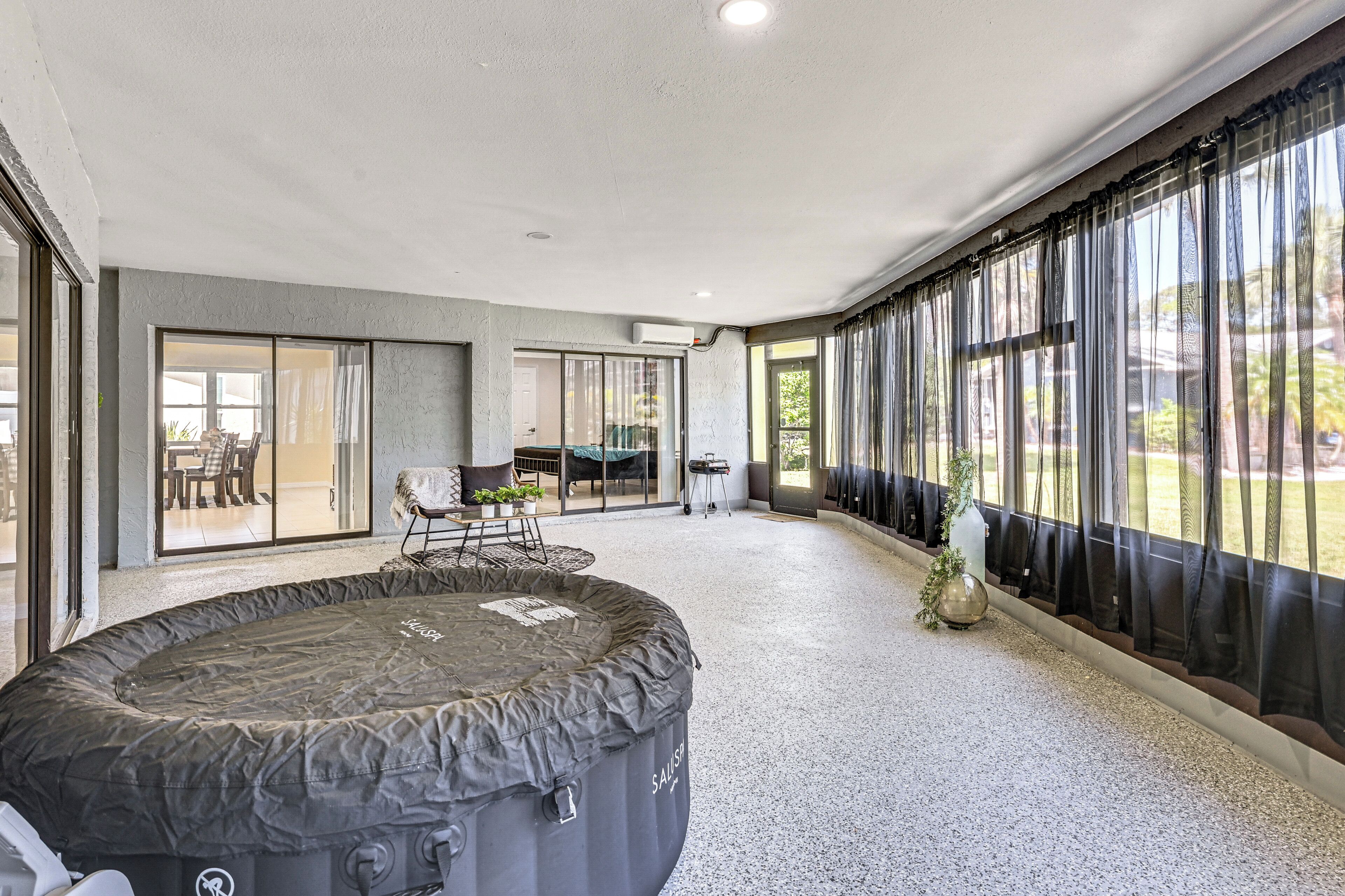 Un espacio interior amplio con un jacuzzi, una mesa de comedor con sillas y vistas a través de grandes ventanales.