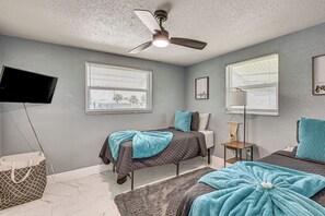 Une chambre avec deux lits, un ventilateur de plafond, une télévision et une fenêtre avec des stores.