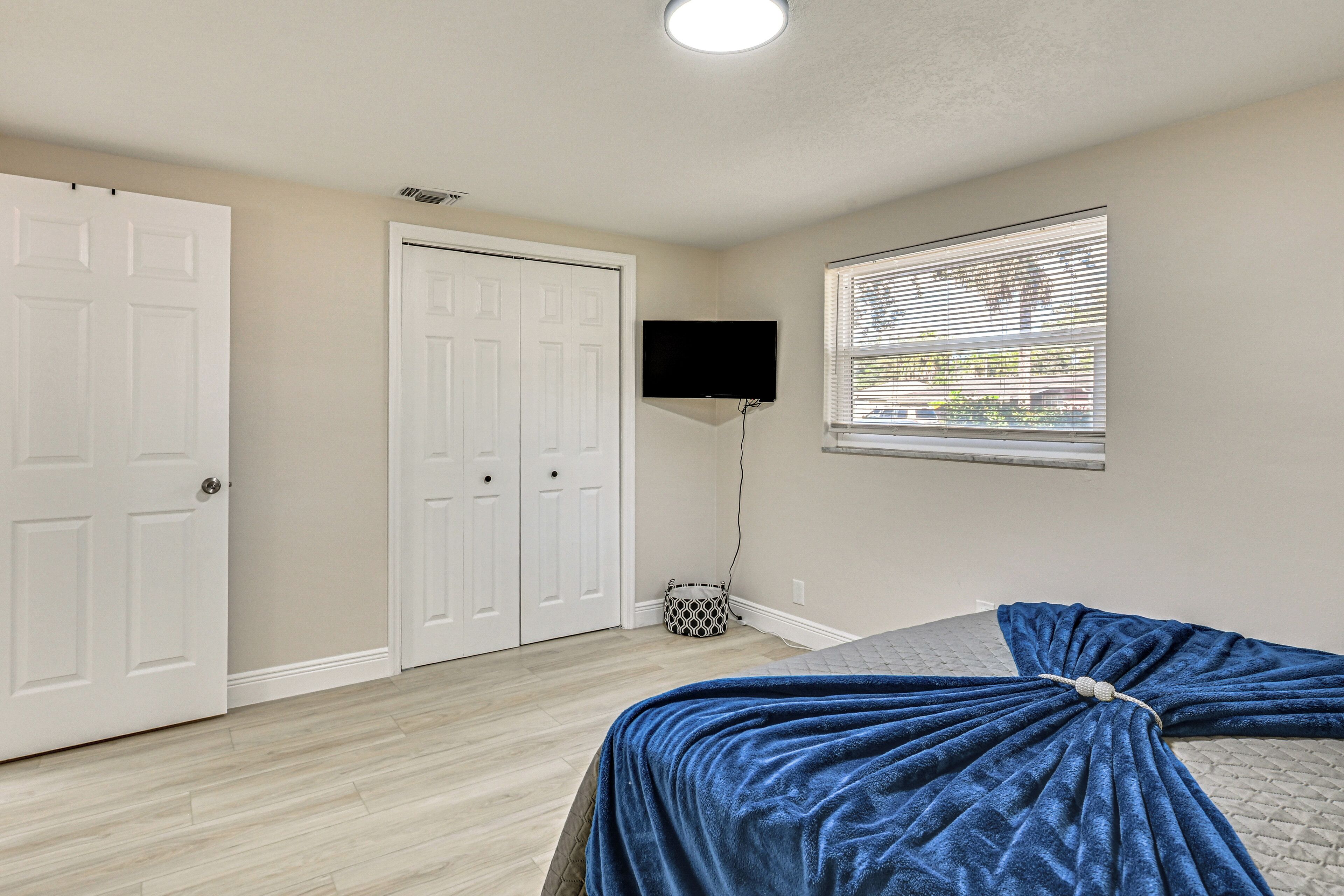 Une chambre à coucher avec un lit, une télévision, une fenêtre avec des stores et une porte.