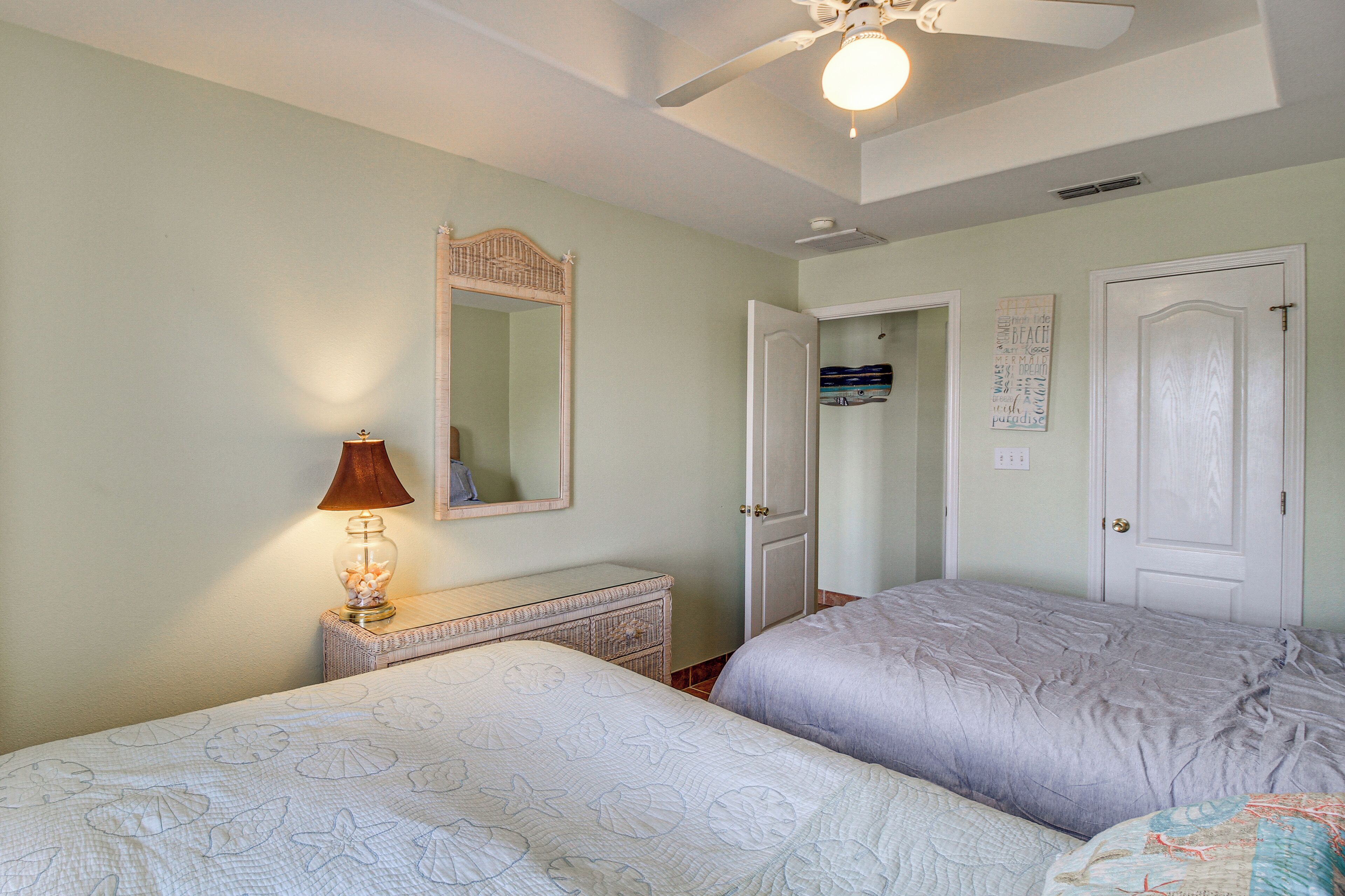 Une chambre avec deux lits, une commode, un miroir et un ventilateur de plafond.