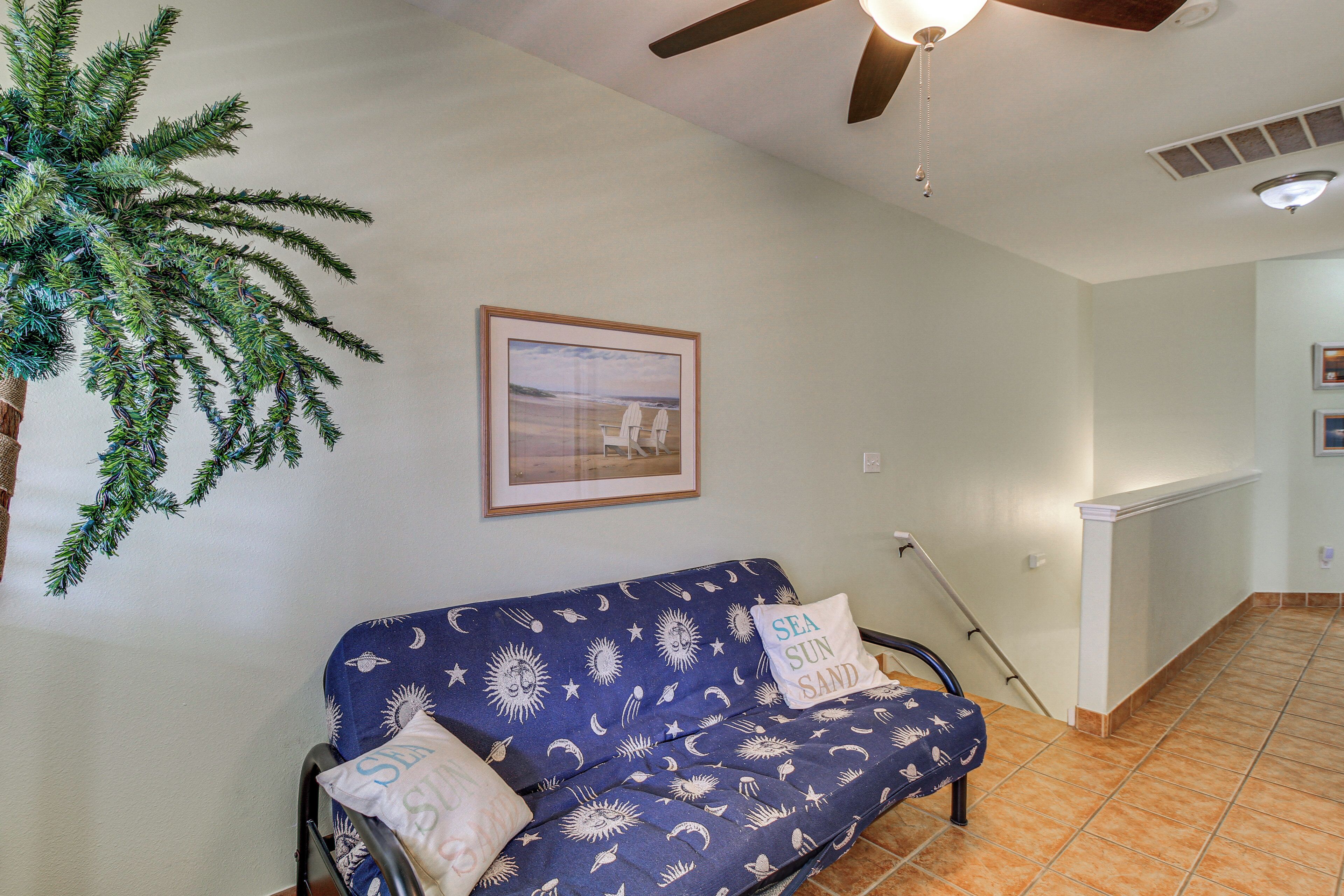 Une pièce avec un canapé bleu, un ventilateur de plafond, un tableau encadré et un radiateur.