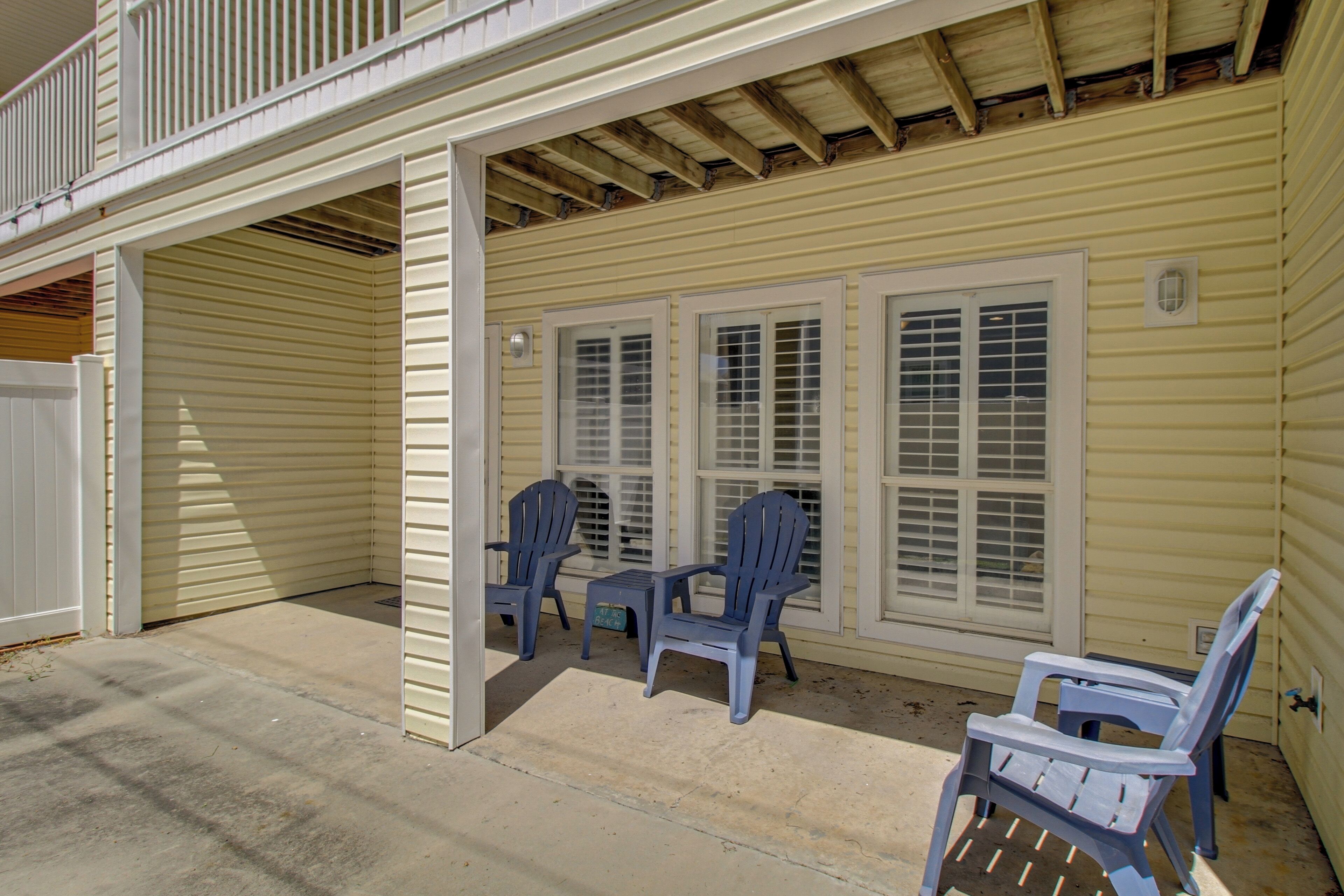A covered outdoor area with a concrete floor, two blue plastic chairs, and a white door.