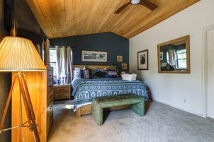 Un dormitorio con techo de madera, una cama con colcha estampada, un banco, una lámpara y un aparador.