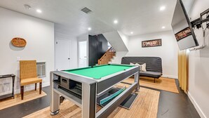 A modern living room with a pool table, a sofa, a chair, and a staircase leading to another level. - Spacious Kanab Basecamp Game Rm, Patio, Fire Pit (Kanab)