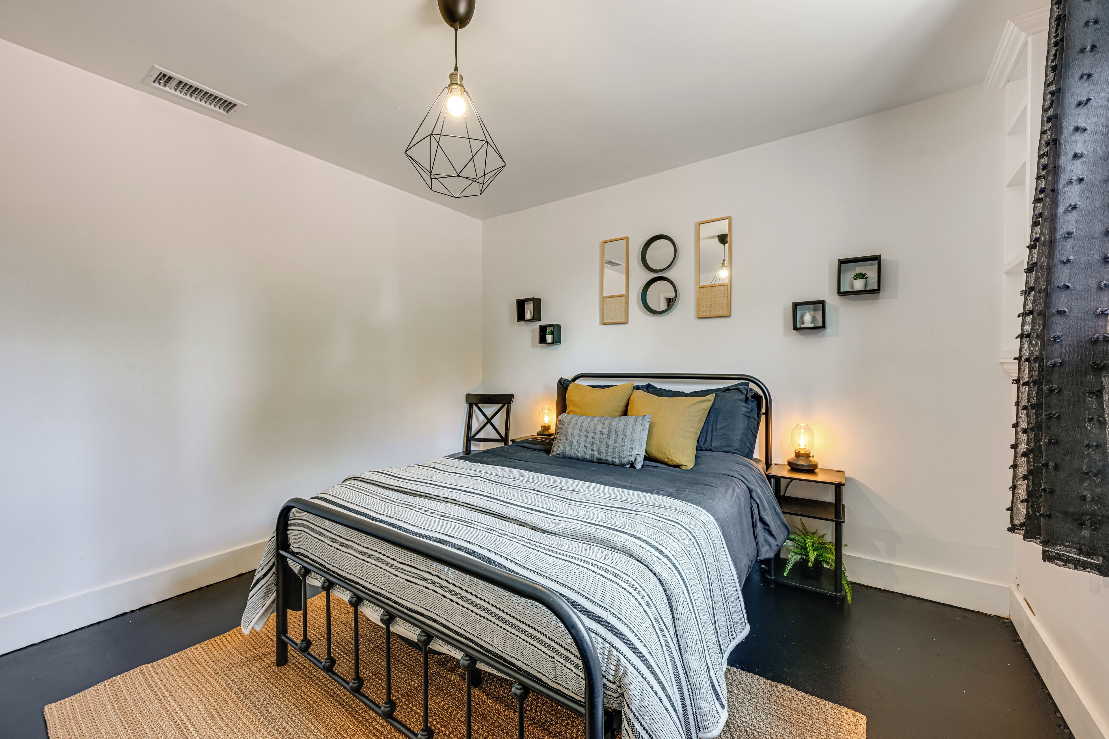 A bedroom with a bed, bedside tables, a hanging light fixture, and wall-mounted mirrors.