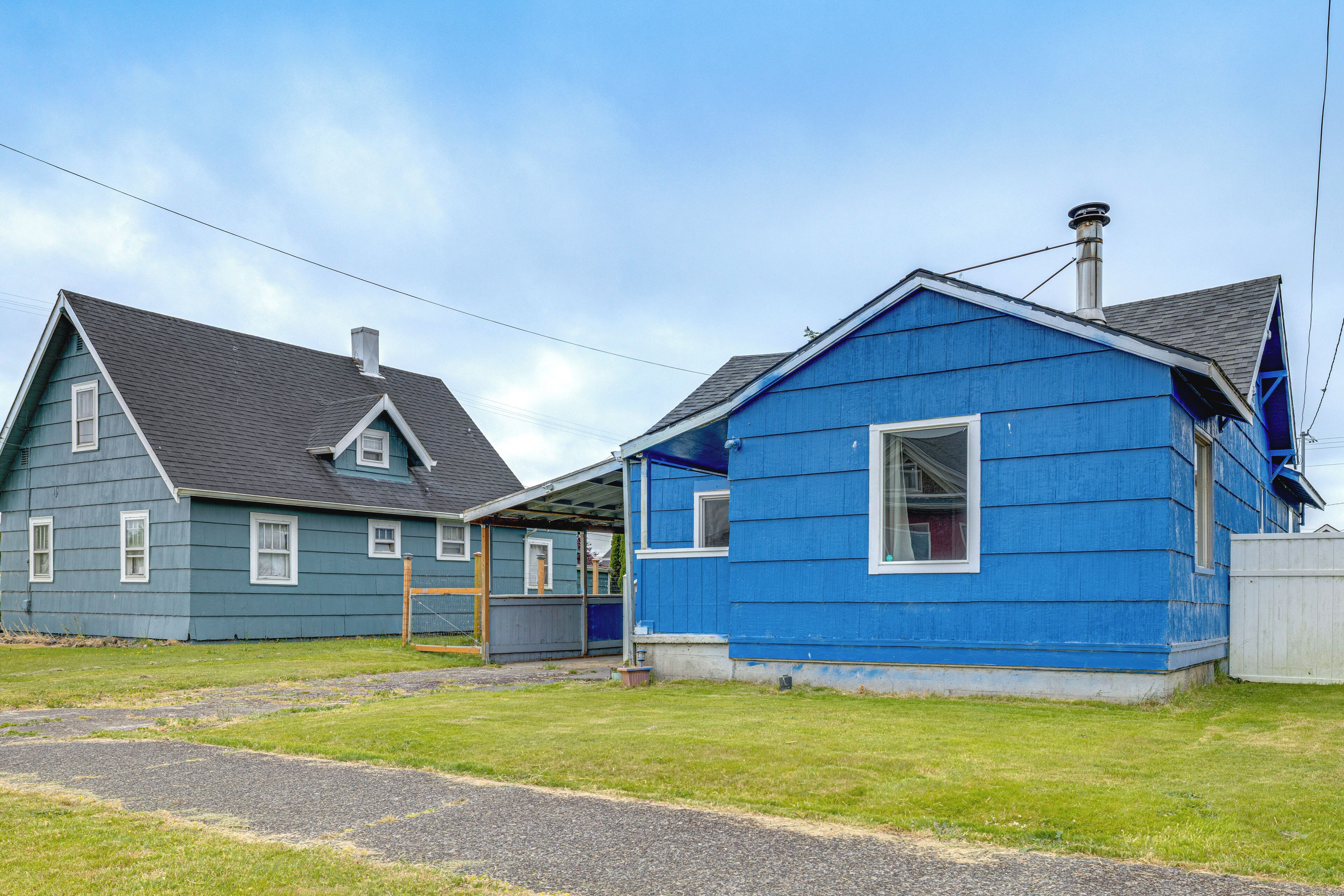 Two houses, one blue and one grey, with a grassy yard and a paved path.
