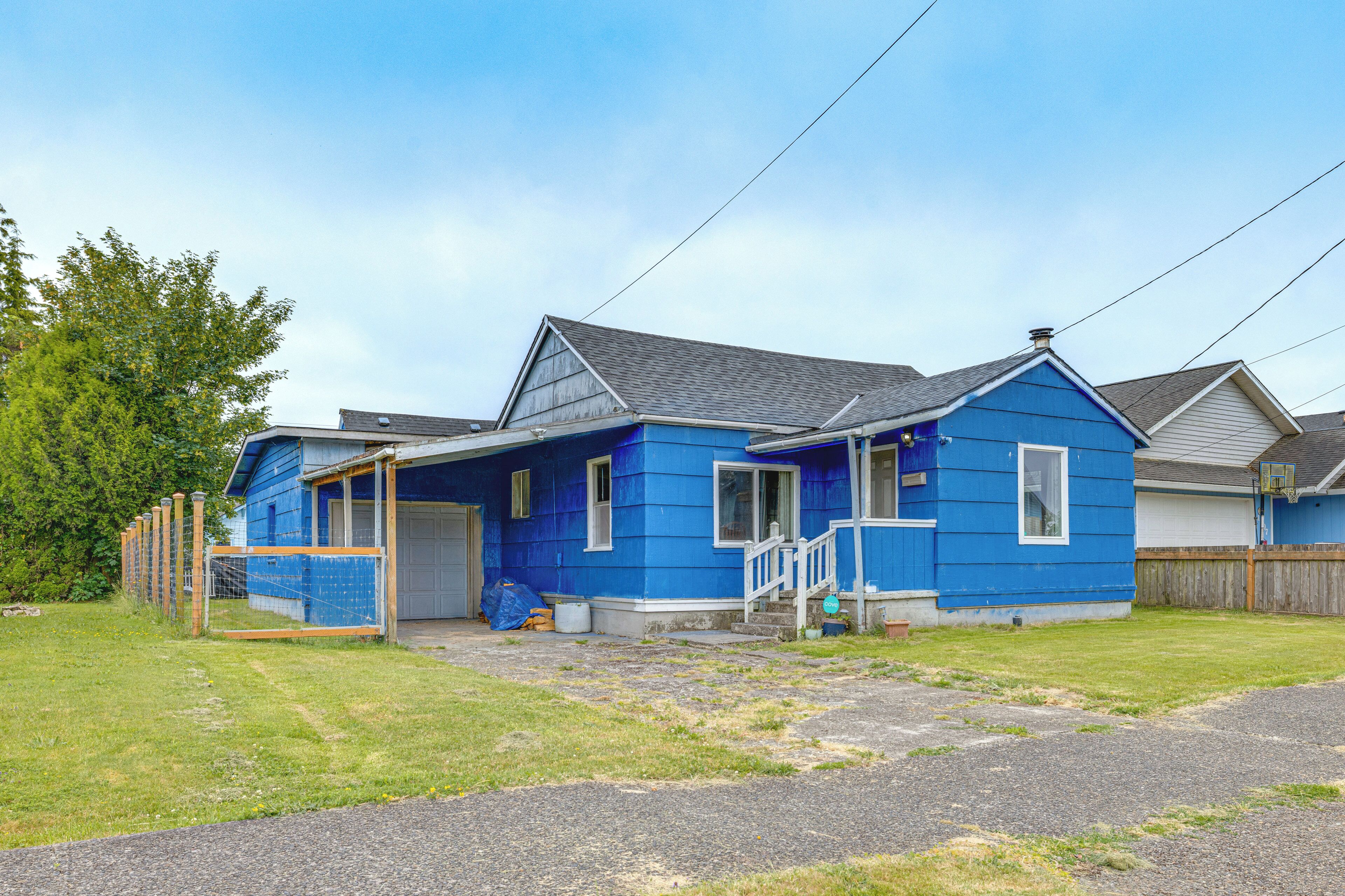 Una casa residencial con fachada azul, un porche delantero y una puerta de garaje visible.