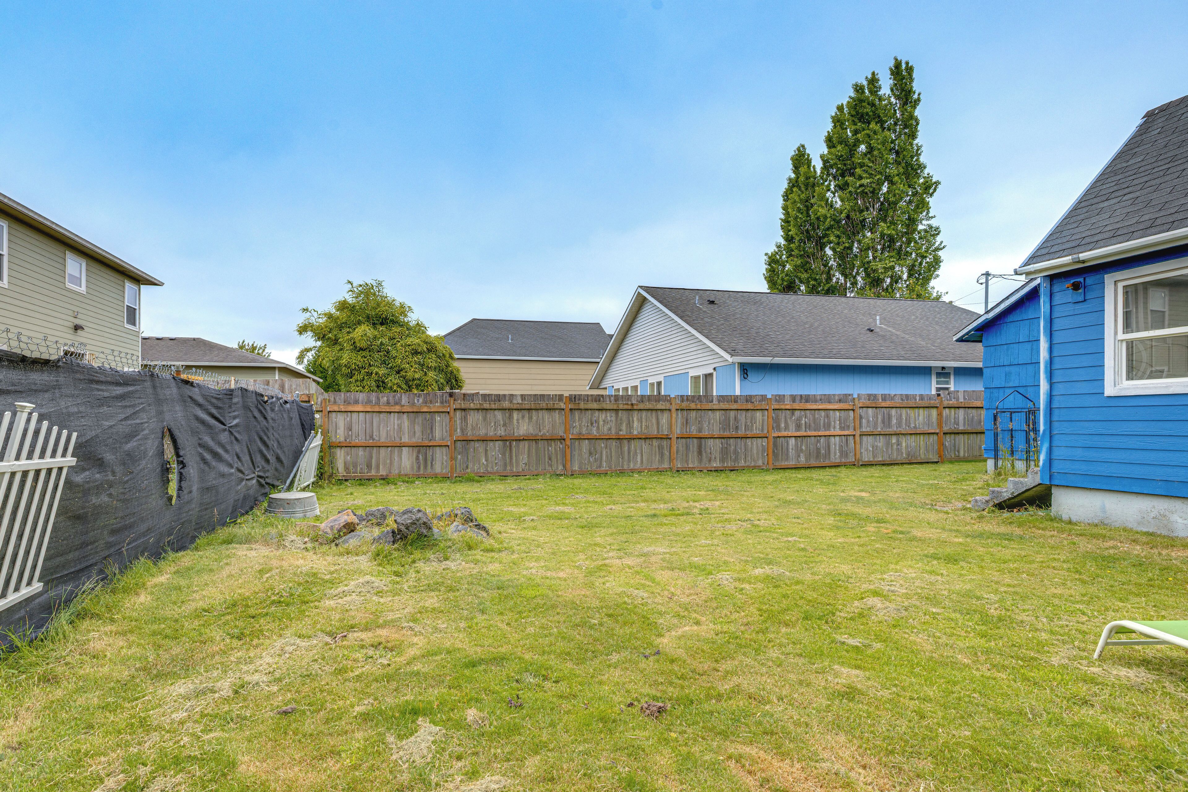 A backyard with a wooden fence, a blue house, and a tree.