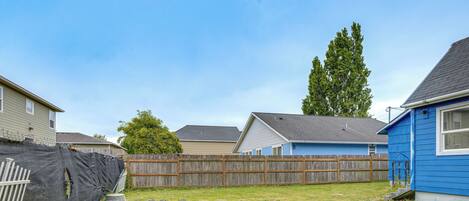 A backyard with a wooden fence, a blue house, and a tree.