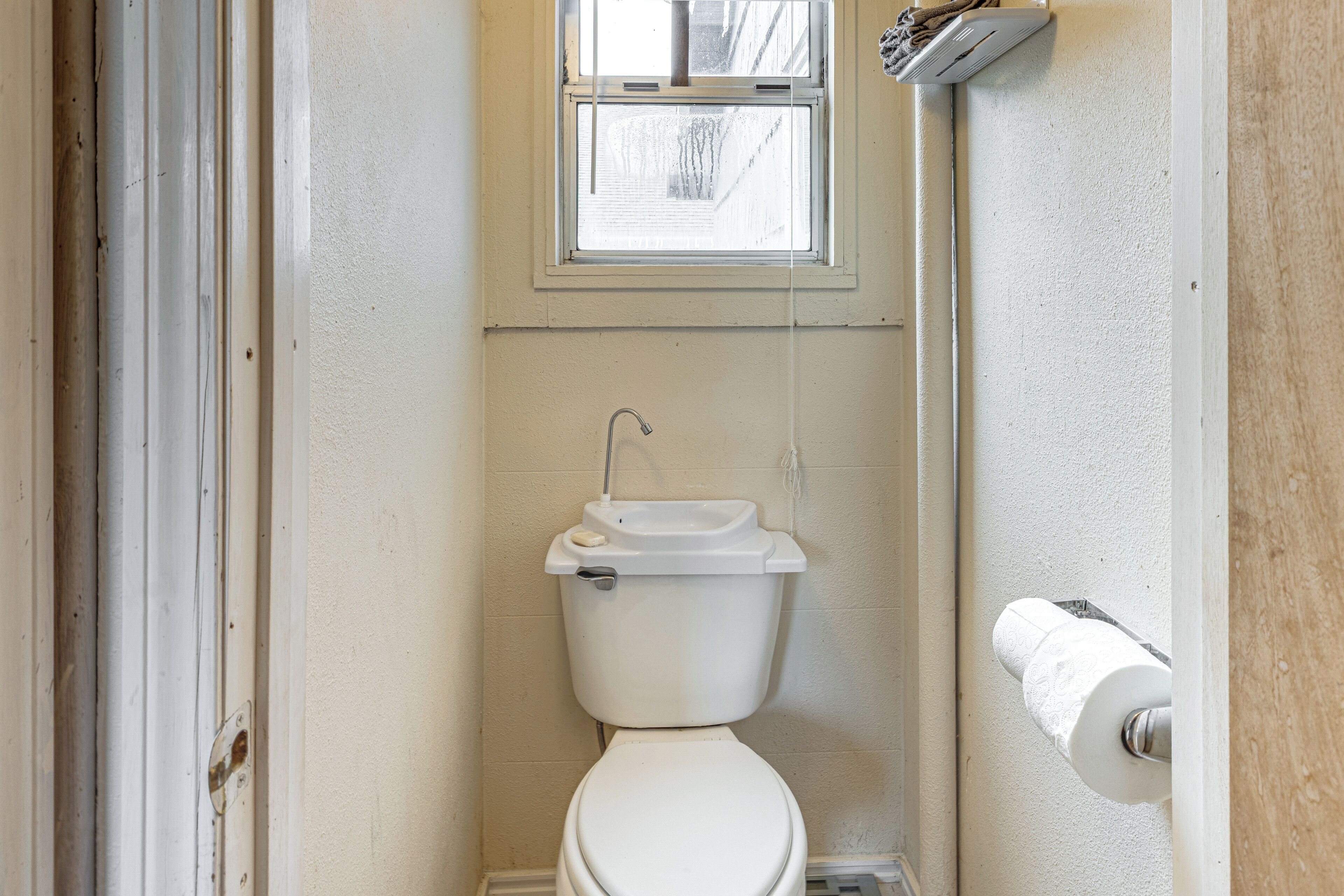 A small, clean bathroom with a toilet, a window, and a visible pipe.